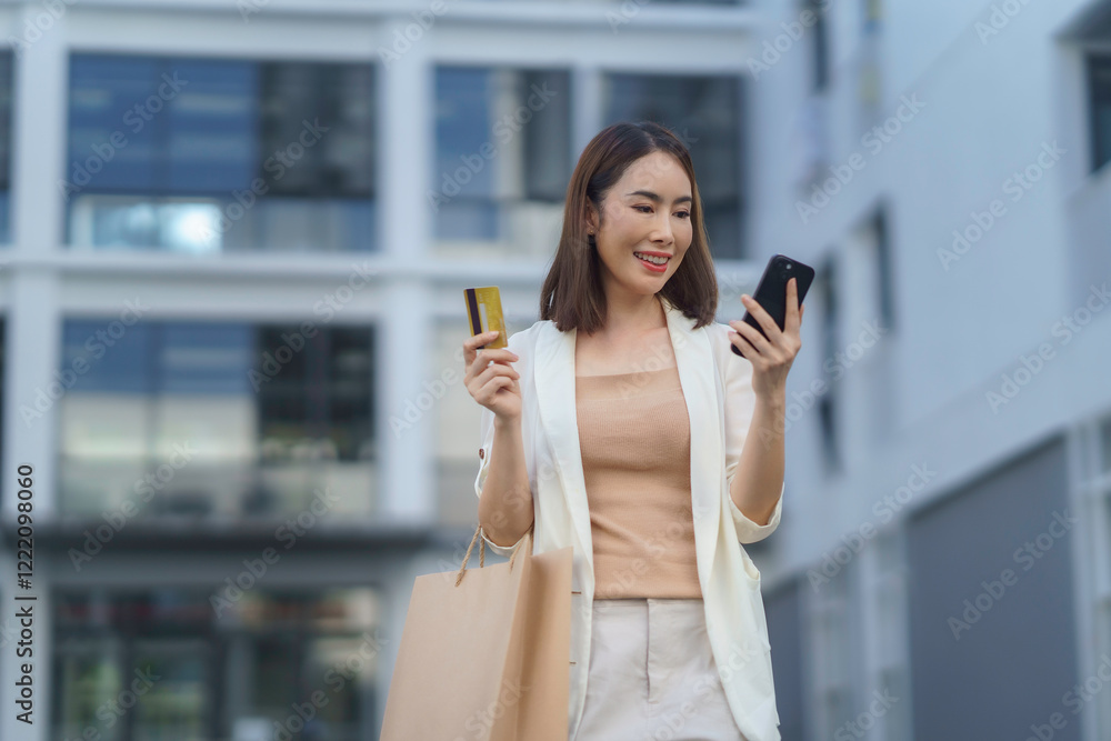 Young business woman using smartphone and credit card, holding shopping bag in the city