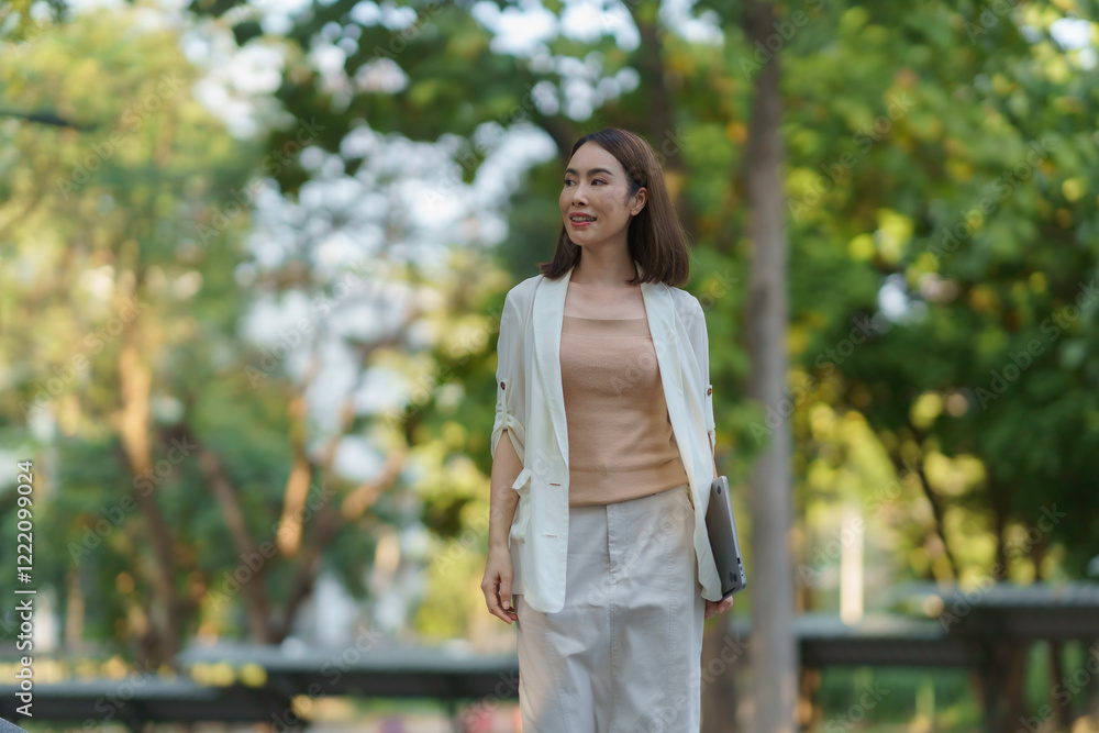 Businesswoman walking in a park holding a laptop and smiling Businesswoman walking in a park holding a laptop and smiling
