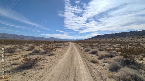 A straight desert road under a vast blue sky with scattered clouds.