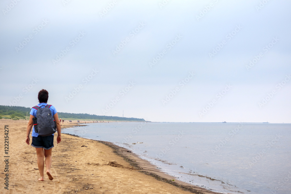 a man walking alone on a wide, sandy beach, with other people in the background and a forest in the distance. a man walking alone on a wide, sandy beach, with other people in the background and a forest in the distance.