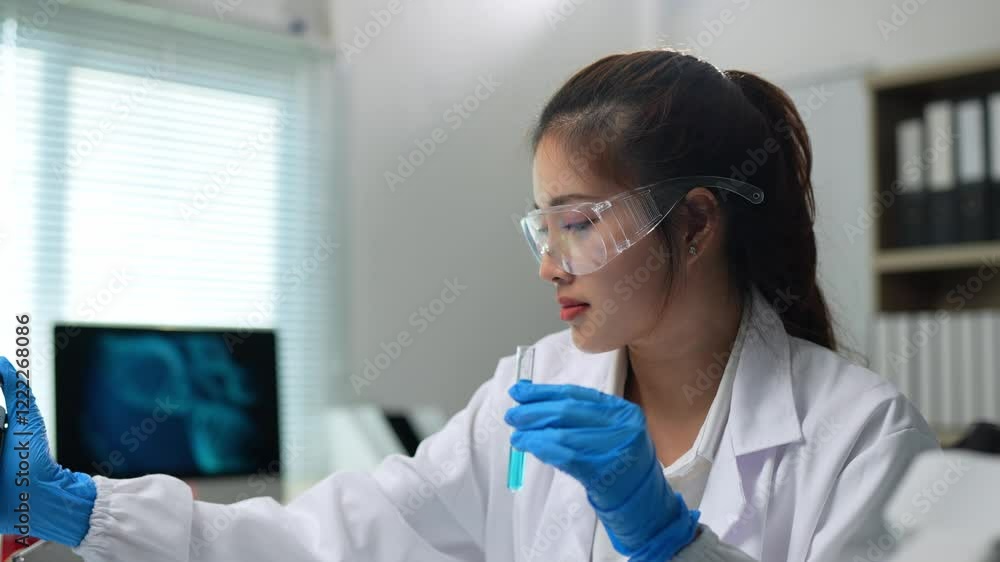Laboratory technician wearing lab coat, safety glasses and gloves, using a pipette to analyze a blue liquid in a test tube in a modern laboratory Laboratory technician wearing lab coat, safety glasses and gloves, using a pipette to analyze a blue liquid in a test tube in a modern laboratory
