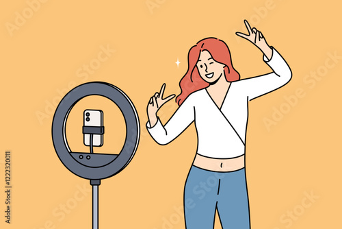 Woman blogger dances in front of phone on tripod with ring lamp, ready-made video for social networks. Video blogger girl smiles while broadcasting live for subscribers and fans from internet.