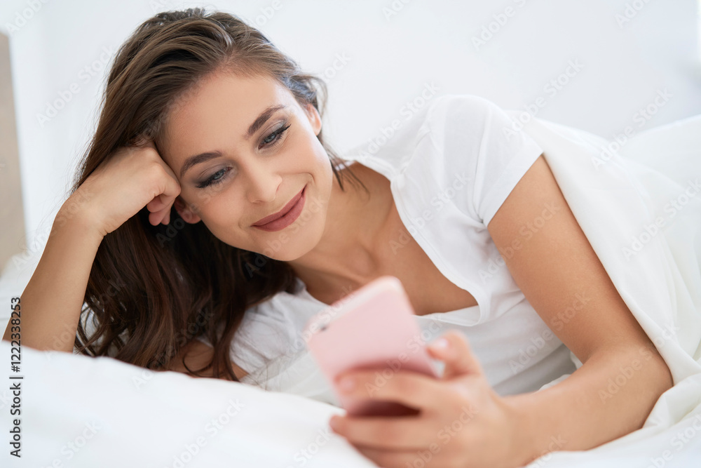 Young woman lying on bed, using smartphone Young woman lying on bed, using smartphone
