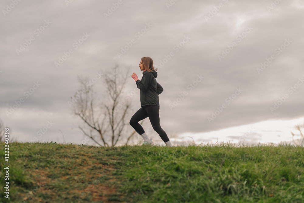 Young woman running outdoors on grassy hill under cloudy sky Young woman running outdoors on grassy hill under cloudy sky