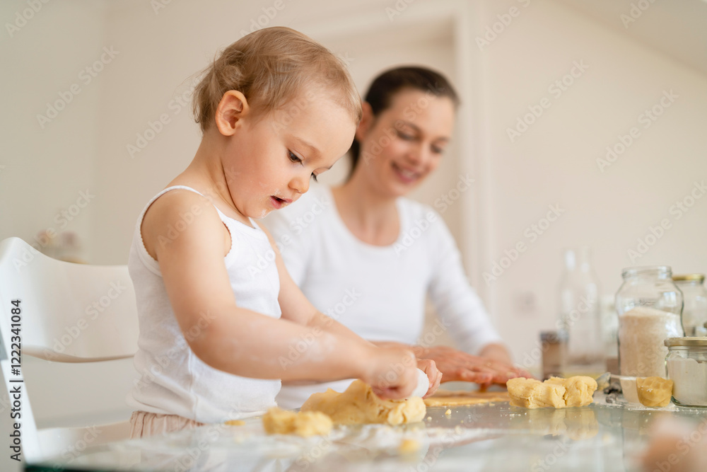 Mother and little daughter with dough roll making a cake together in kitchen at home Mother and little daughter with dough roll making a cake together in kitchen at home