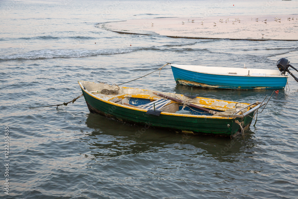 Two weathered boats anchored in calm waters during the early morning light near a serene shoreline Two weathered boats anchored in calm waters during the early morning light near a serene shoreline