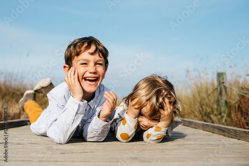 Portrait of laughing boy and his little sister lying side by side on boardwalk photo