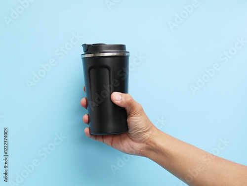Male hand holding black thermos mug or thermos on blue background side view.