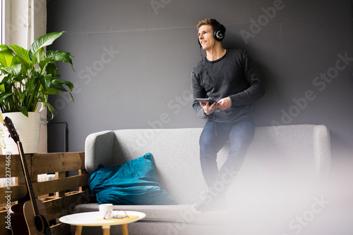 Relaxed young man with tablet and guitar listening to music with headphones photo