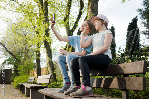 Two girls sitting on a park bench taking a selfie photo