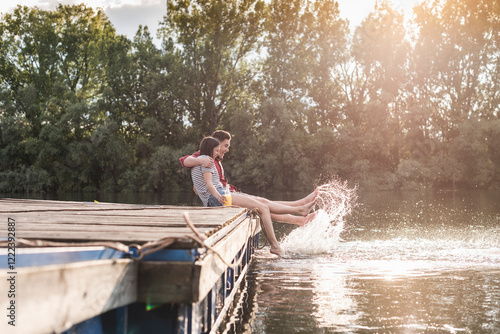 Happy young couple having a drink and splashing with water on jetty at a remote lake photo