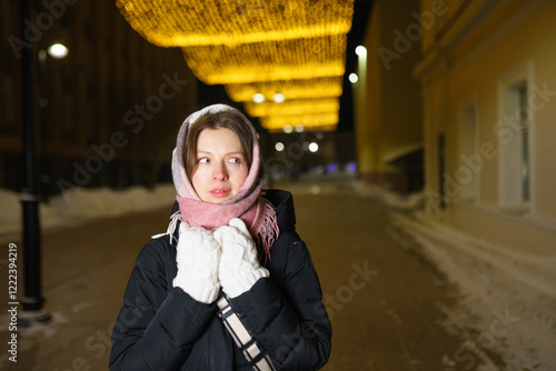 Pensive woman in warm clothes walking on street at night photo