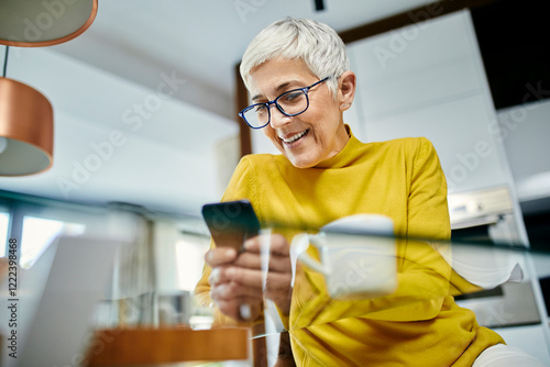 Senior woman drinking coffee, checking text messages on her smartphone photo