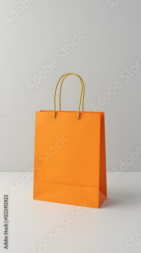 Bright orange shopping bag with gold handles on light grey background is a versatile template for showcasing branding or product design. Stylish and minimalistic look.