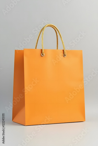 Bright orange shopping bag with gold handles on light grey background is a versatile template for showcasing branding or product design. Stylish and minimalistic look.