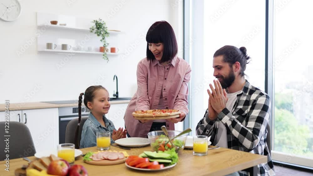 Caucasian family gathered in kitchen for breakfast with pizza, mother, father, young daughter sharing meal at table with orange juice, fruits, vegetables, cheerful atmosphere promoting family bonding. Caucasian family gathered in kitchen for breakfast with pizza, mother, father, young daughter sharing meal at table with orange juice, fruits, vegetables, cheerful atmosphere promoting family bonding.