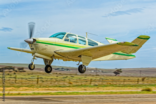 Light aircraft six-seat with green stripes and retracting undercarriage and unique V shaped tail taking off from an airstrip in the Western Cape, South Africa