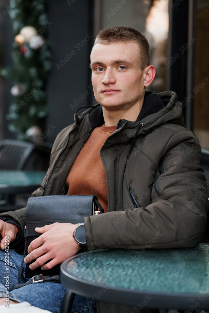 Young man in a casual outfit sitting at an outdoor cafe table, exuding confidence and style Young man in a casual outfit sitting at an outdoor cafe table, exuding confidence and style