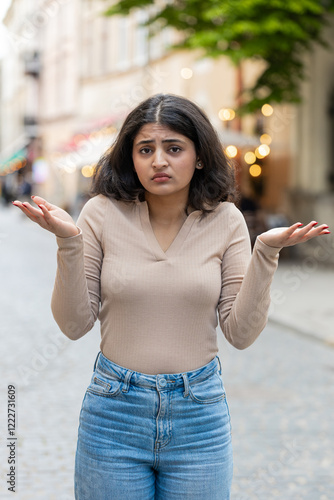 What. Why. Surprised frustrated Indian woman raising hands asking reason of failure demonstrating disbelief irritation by troubles outdoors. Confused girl walking on urban city street. Vertical photo