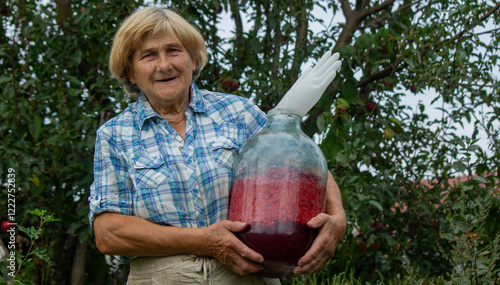Foto Elderly Woman Holding a Glass Bottle with Raspberries in the Garden