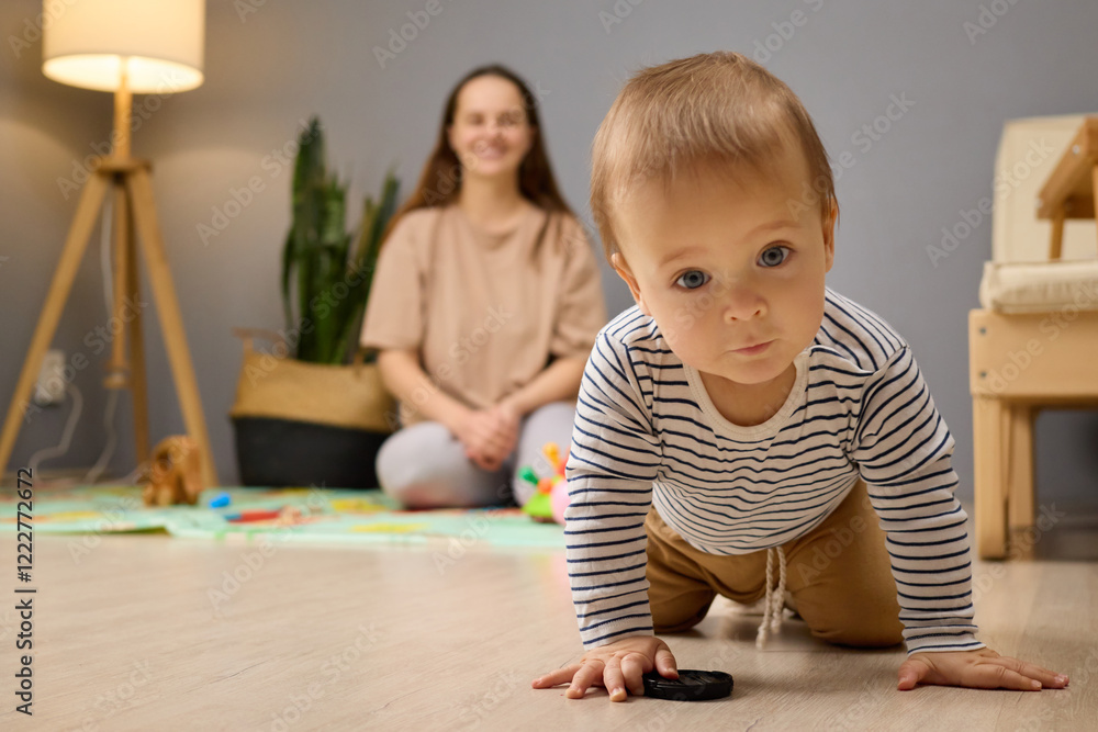 A young child crawls towards a small toy on the floor. A mother watches lovingly from a nearby chair, creating a warm and nurturing atmosphere in a well-lit living room A young child crawls towards a small toy on the floor. A mother watches lovingly from a nearby chair, creating a warm and nurturing atmosphere in a well-lit living room