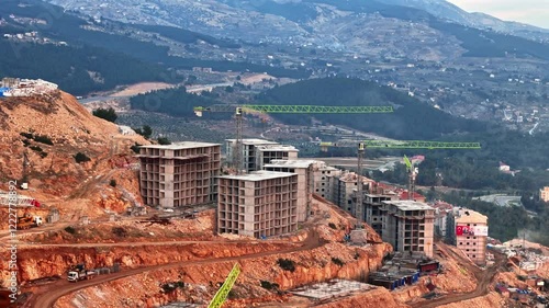 The video shows a multi-story residential construction site. Buildings are at different stages; some in the rough construction phase. The site includes roads, material areas,situated on a hillside. photo