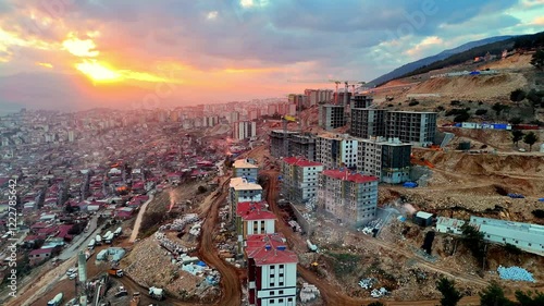 The video shows a multi-story residential construction site. Buildings are at different stages; some in the rough construction phase. The site includes roads, material areas,situated on a hillside. photo