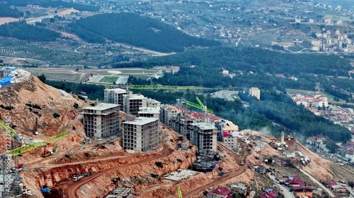 The video shows a multi-story residential construction site. Buildings are at different stages; some in the rough construction phase. The site includes roads, material areas,situated on a hillside. photo