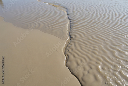 Beach stream meeting ocean with rippled sand patterns