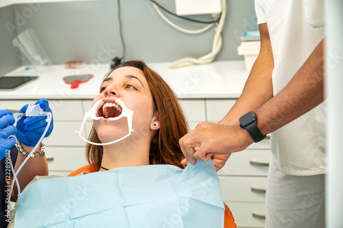 Tableau sur toile Young woman undergoing dental examination with mouth retractor and dental tools