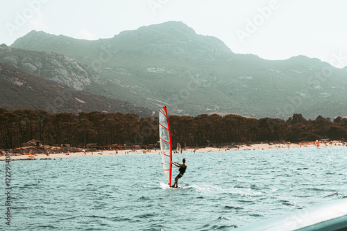 Surf à voile au large de la côte Corse en plein été, fond de plage et massif montagneux, vu d'un bateau au large