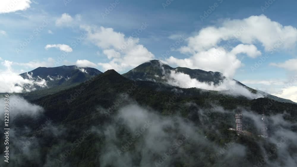 Aerial view of beautiful mountain peak with lush green tropical forest in morning mist. Clouds move in the wind at Puncak Bogor. Aerial view of beautiful mountain peak with lush green tropical forest in morning mist. Clouds move in the wind at Puncak Bogor.