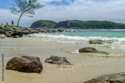 Alignment of large stones embedded in the sand, with sea and mountains in the background. Photographed on Conchas beach, Cabo Frio, Rio de Janeiro, Brazil.