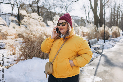 Happy 30s woman talking phone and look happy outdoors. Urban lifestyle concept. Winter time. Beautiful woman walking on the modern city public park.