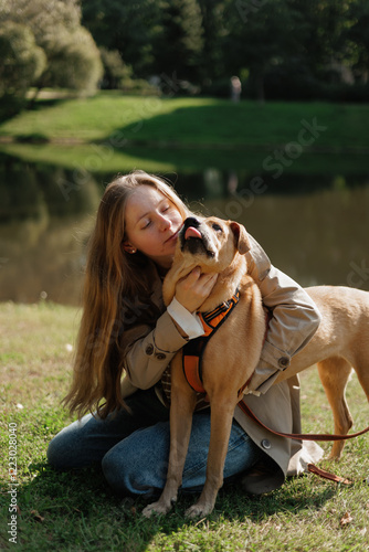 young woman walks with her dog in the park. A lady in a beige raincoat is playing with a pit bull on a green lawn. animal and human friendship, pet training, female dog handler or zoopsychologist photo