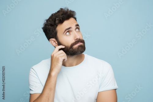 Young Man Biting Nails. Portrait of Confused Adult Guy in Casual T-Shirt, Isolated on Pastel Blue Background. People Lifestyle Concept photo