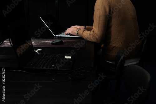 dettaglio di un giovane uomo adulto italiano irriconoscibile sullo sfondo, vestito con abiti casual e moderni, che lavora al computer, seduto alla scrivania, in un ufficio photo