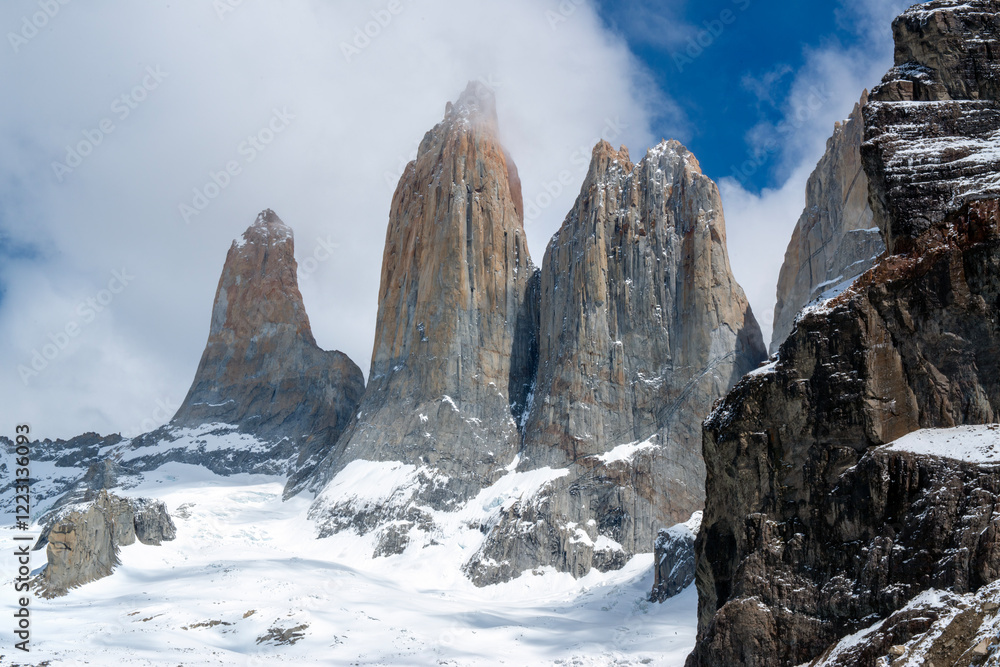 Obraz premium The three famous snow-capped towers of the Torres del Paine National Park massif stand out against a blue sky and white clouds.