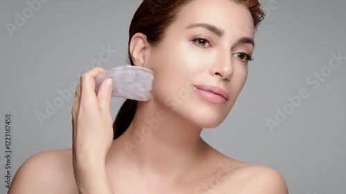 Natural beauty woman using gua sha tool for skincare and anti-aging routine photo