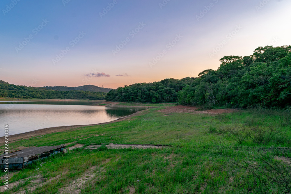 Fototapeta premium Beautiful view of the Várzea das Flores lake, with water lapping the shore, cloudy sky and woods in the background.