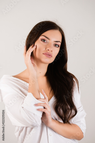 Obraz na płótnie Young woman with dark hair in a white shirt touching the skin of her face w salonie