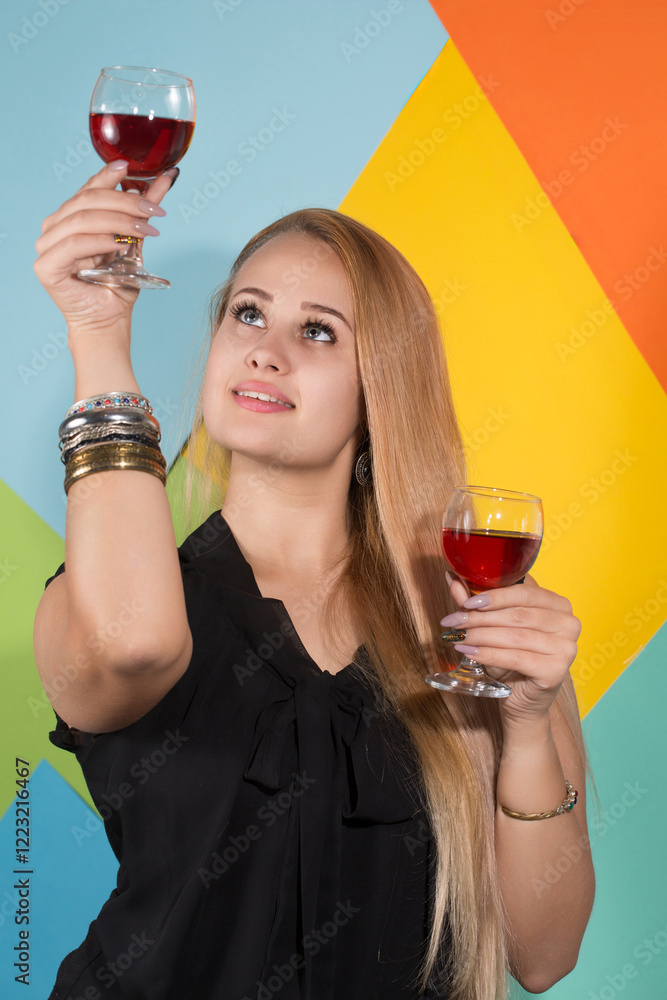 A woman is holding two wine glasses and smiling on a colored geometric background