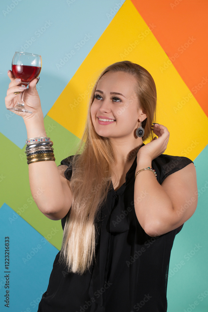 Beautiful blonde in a black dress holding a glass of red wine and looking at the drink and smiles