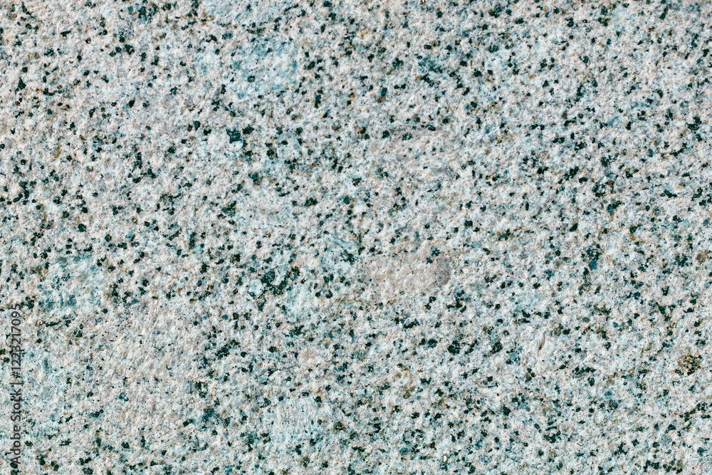 A grey and white stone wall with a few green specks A grey and white stone wall with a few green specks