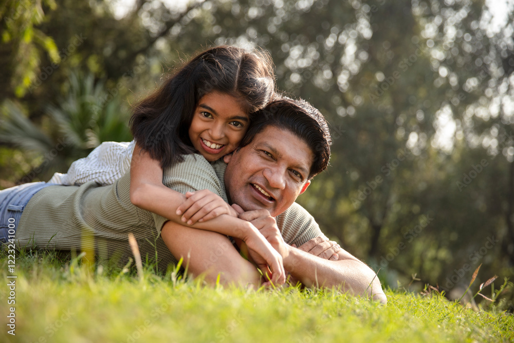 Indian happy father and daughter lying down and embracing, spending leisure time by looking at camera outdoors at park. Concept of indian father and daughter love Indian happy father and daughter lying down and embracing, spending leisure time by looking at camera outdoors at park. Concept of indian father and daughter love