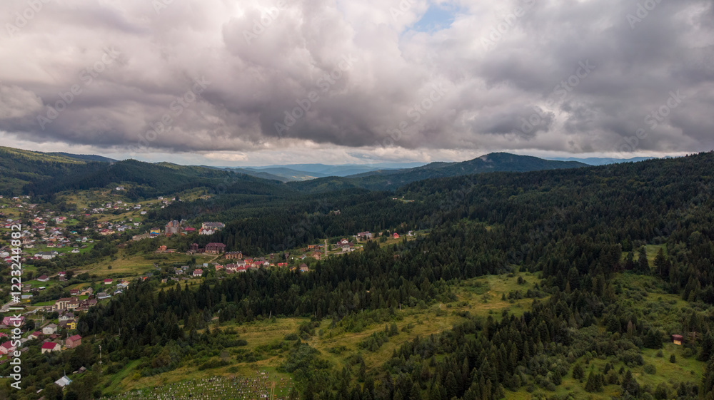 Obraz premium Aerial View Of A City Surrounded By Majestic Mountains Under A Cloudy Sky. The Dramatic Landscape Creates A Stunning Contrast Between Urban Life And Natural Beauty.