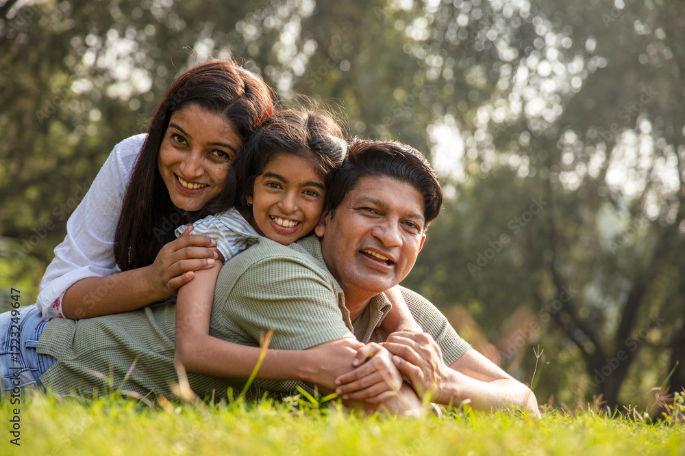 Fototapeta premium Happy Indian family spending leisure time at the nature outdoor park. Happy indian couple with kids embracing by looking at camera at garden. Concept of relationship, togetherness and family lifestyle