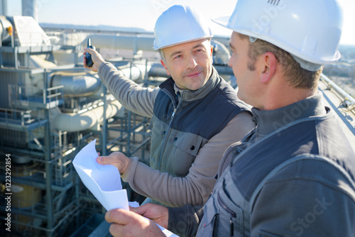 two male workers looking at plans overlooking industrial site photo