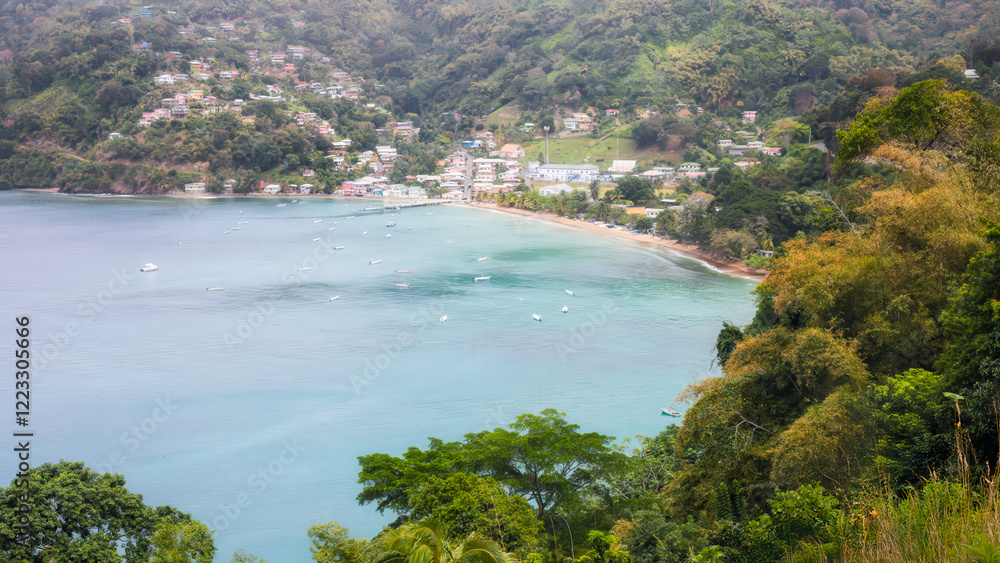 Obraz premium View from above to Charlotteville seaside village with colorful houses, boats in the bay, surrounding rainforest groved hills. Tropical destination in Tobago, Trinidad and Tobago.