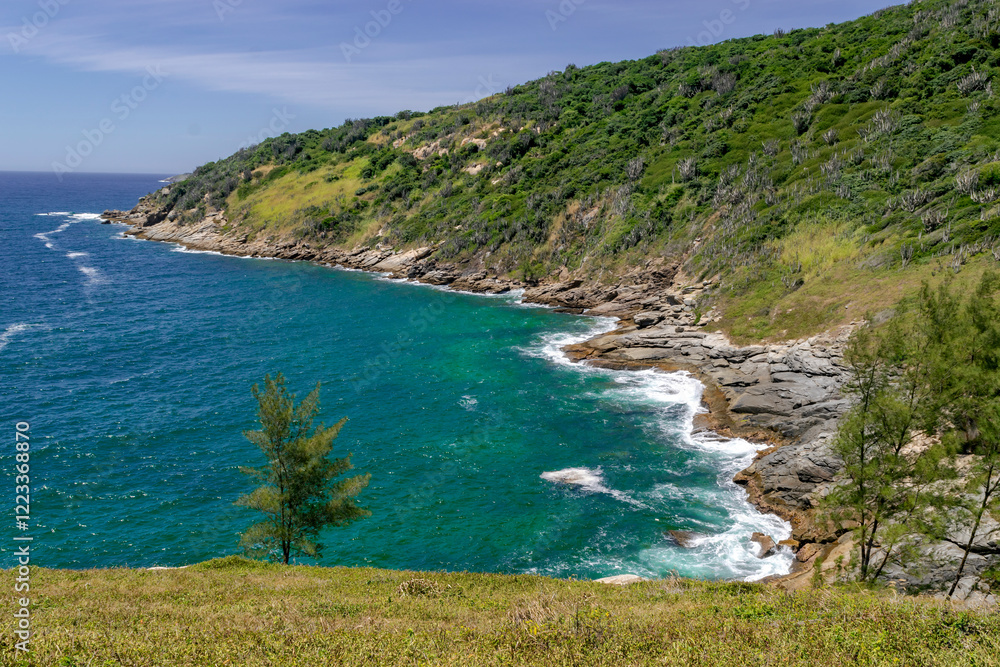 Fototapeta premium View from above of Foguete beach, with blue sea and sky, lots of rocks and mountains around. Cabo Frio, Rio de Janeiro.